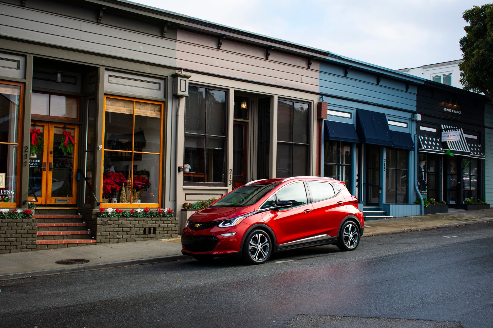 Red electric car parked on a charming street in Pacific Grove, CA, showcasing quaint shops.