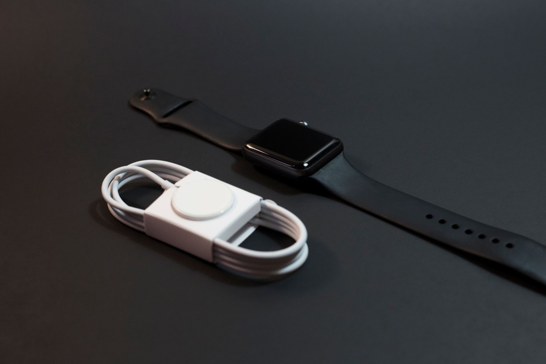Close-up of a black smartwatch and white charging cable on a dark surface. Ideal for technology themes.