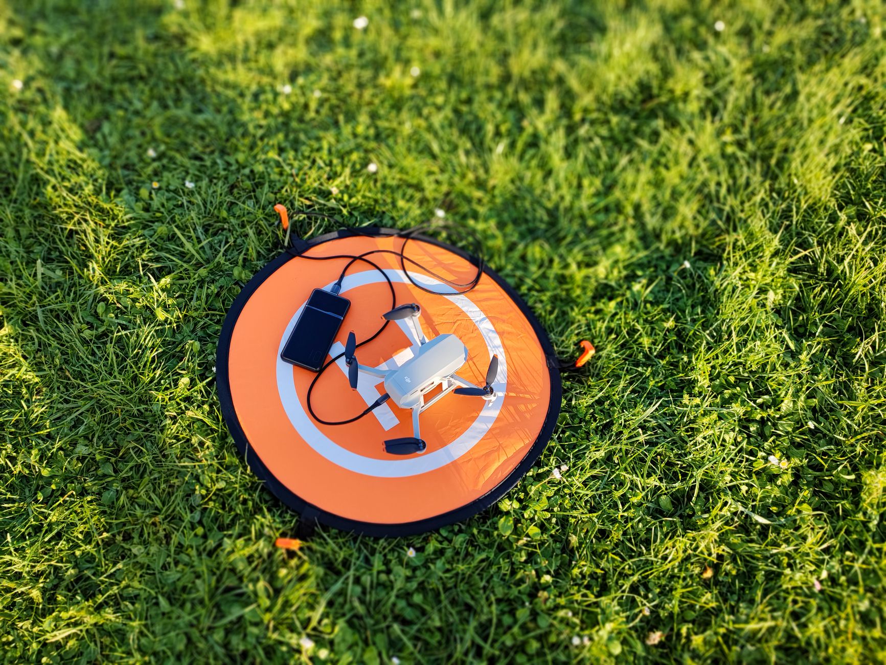 Close-up of a drone and smartphone placed on an orange landing pad in lush green grass.