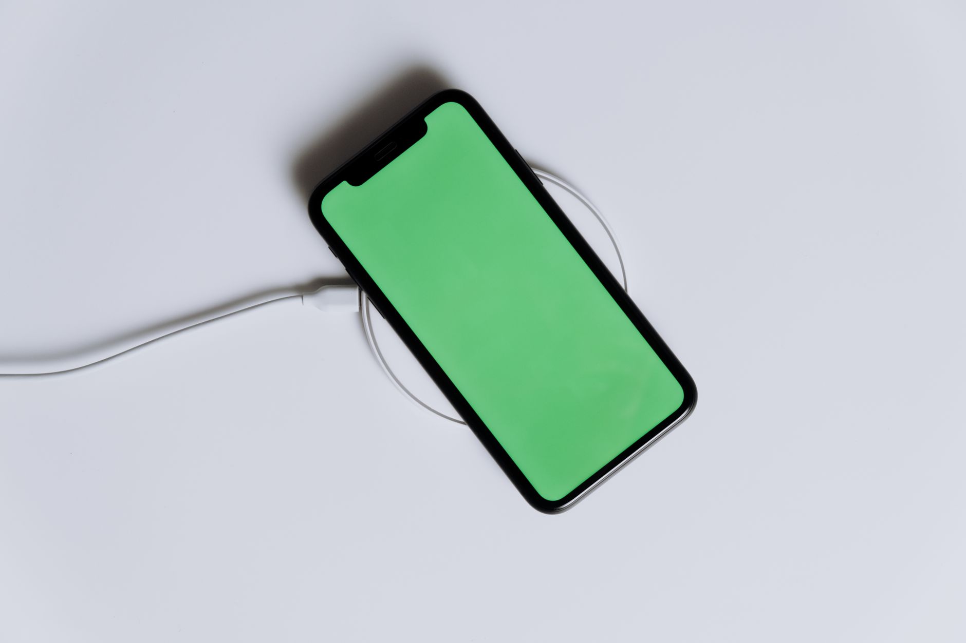 A minimalist smartphone with a green screen on a wireless charger, ideal for tech mockups.