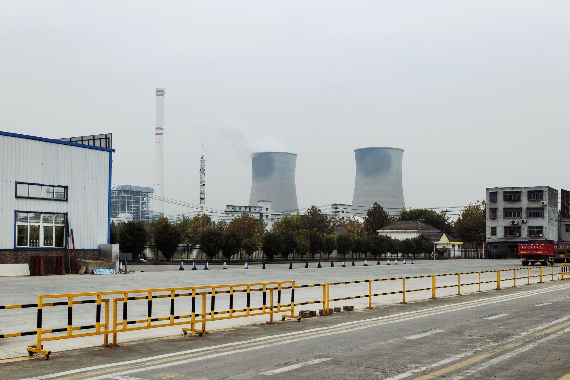 An industrial area with power plant cooling towers emitting smoke under a cloudy sky.