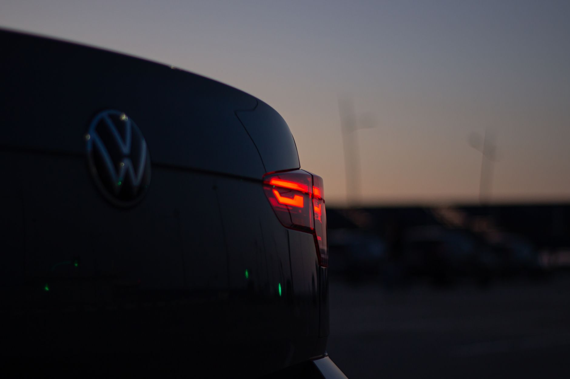 A close-up of a car's taillight glowing red against the evening sky.
