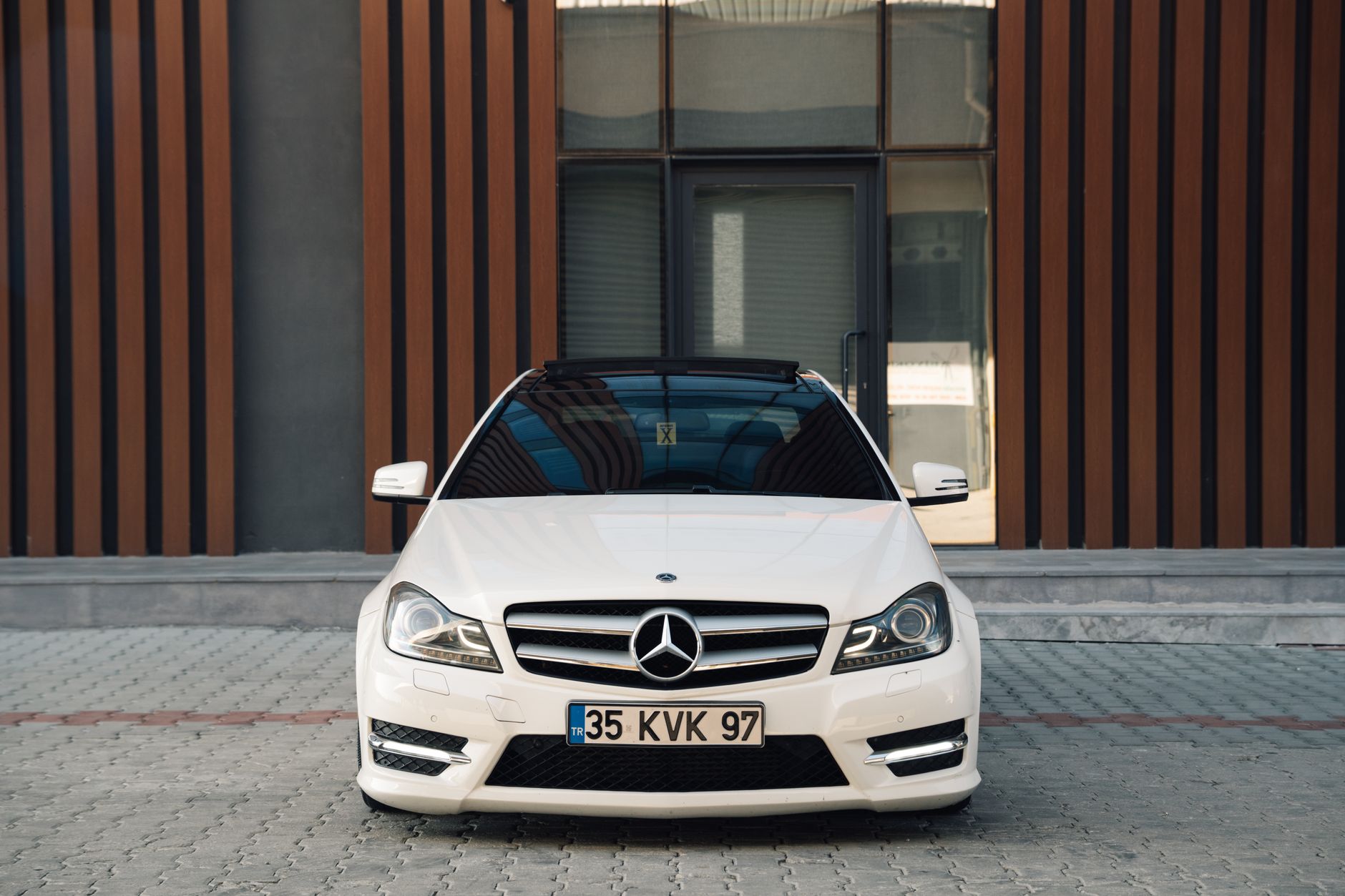 A sleek white Mercedes-Benz C-Class parked in front of a modern building, showcasing luxury design.