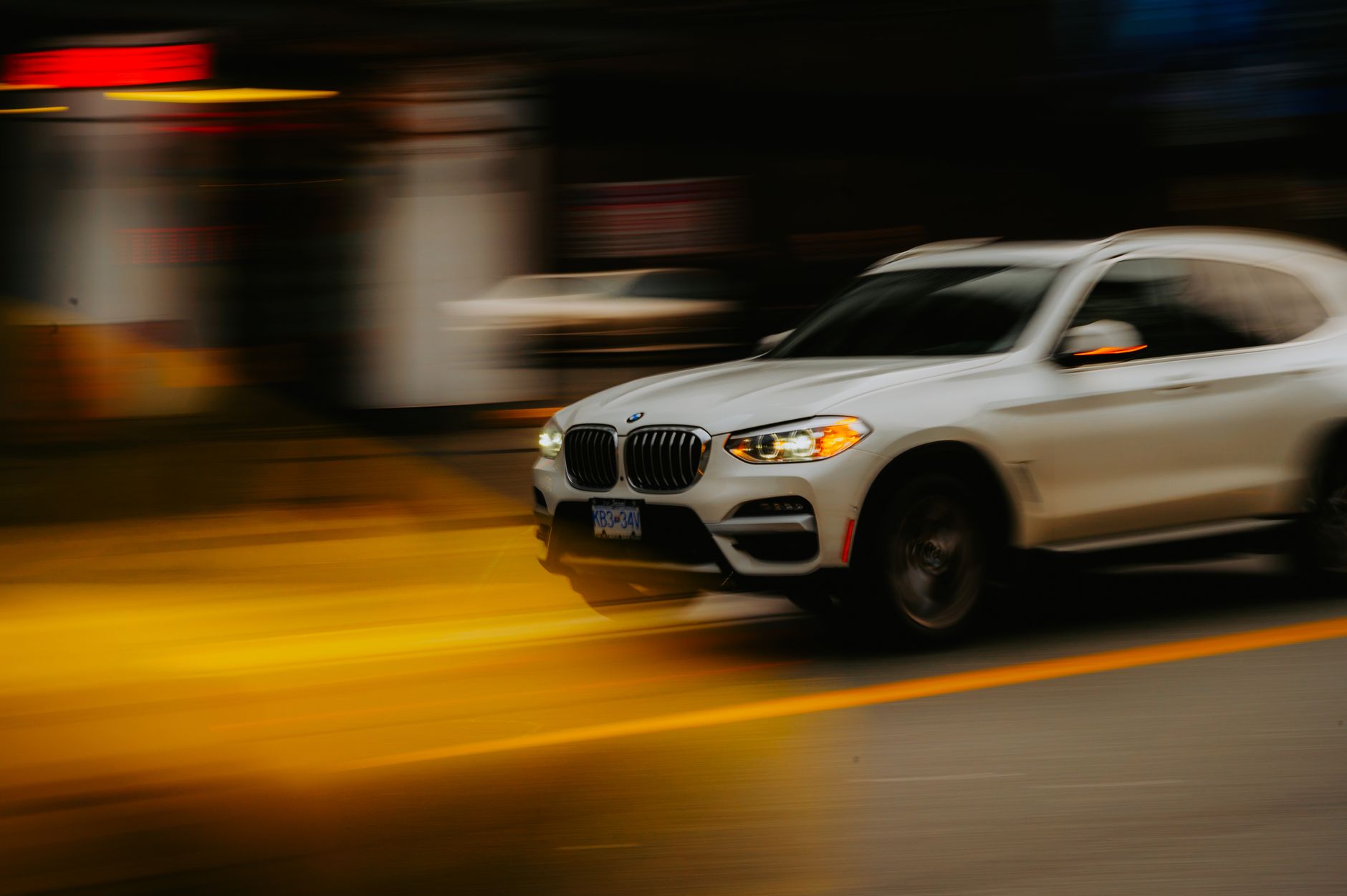 Blurred motion shot of a white BMW SUV speeding through urban city streets.