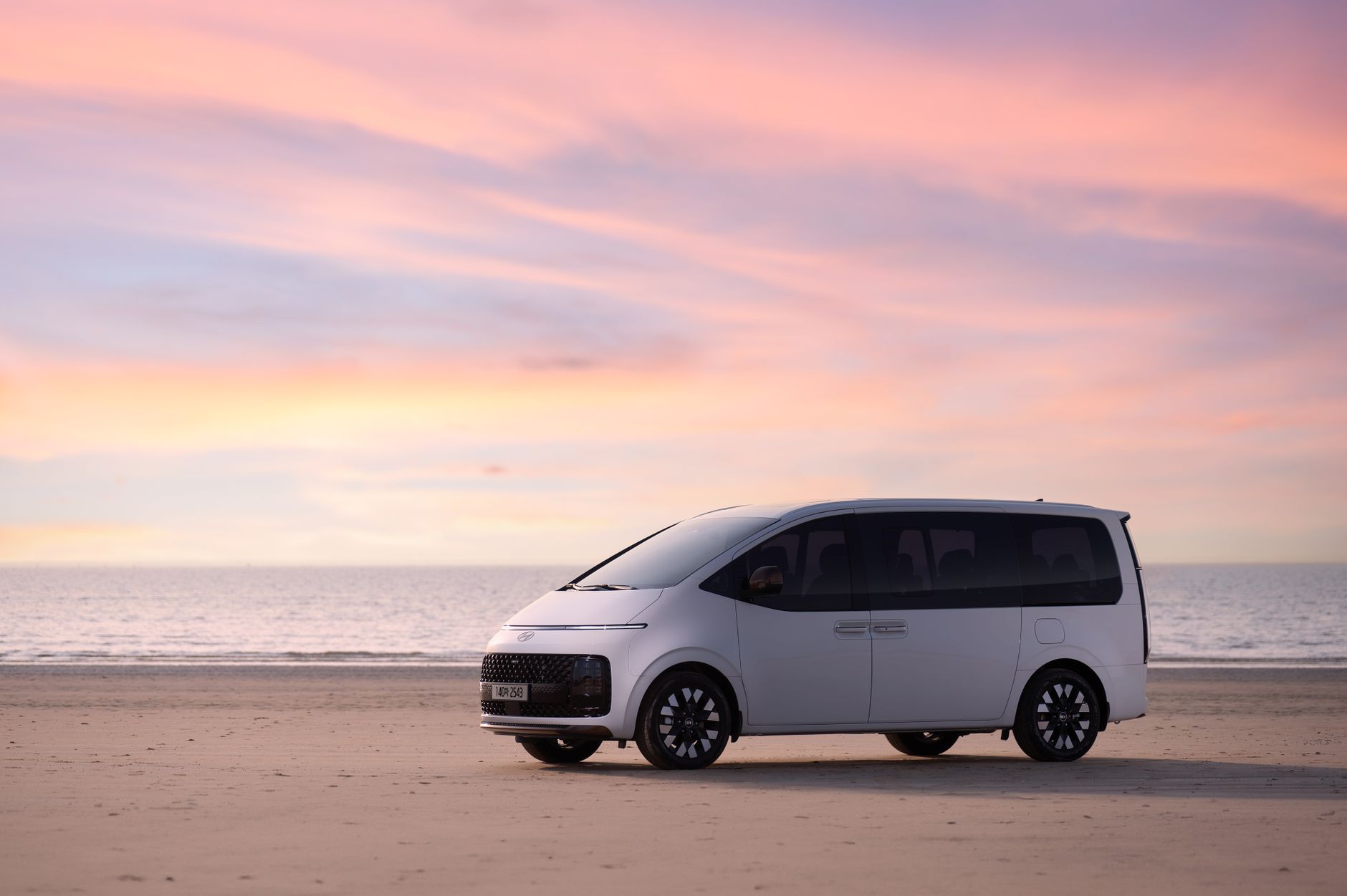 A white minivan on a sandy beach with a stunning pink sunset backdrop.