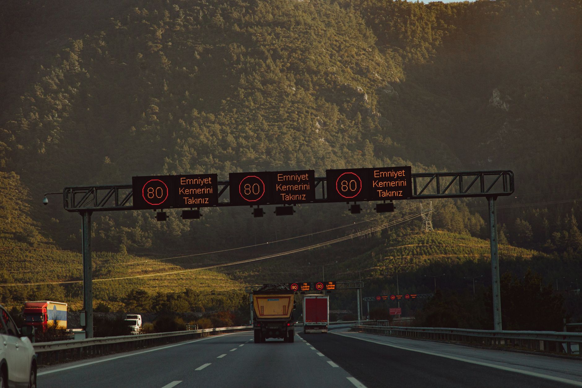 Highway with speed limit signs against a mountainous backdrop and low traffic.