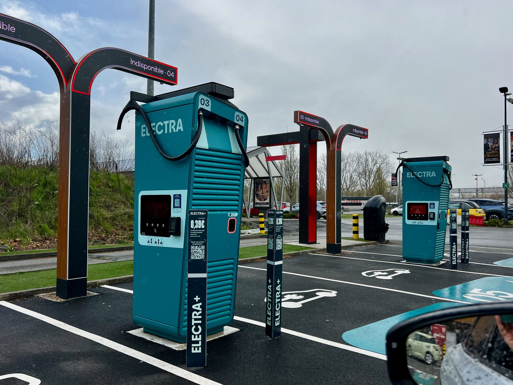 A modern electric vehicle charging station in a parking lot on a cloudy day.