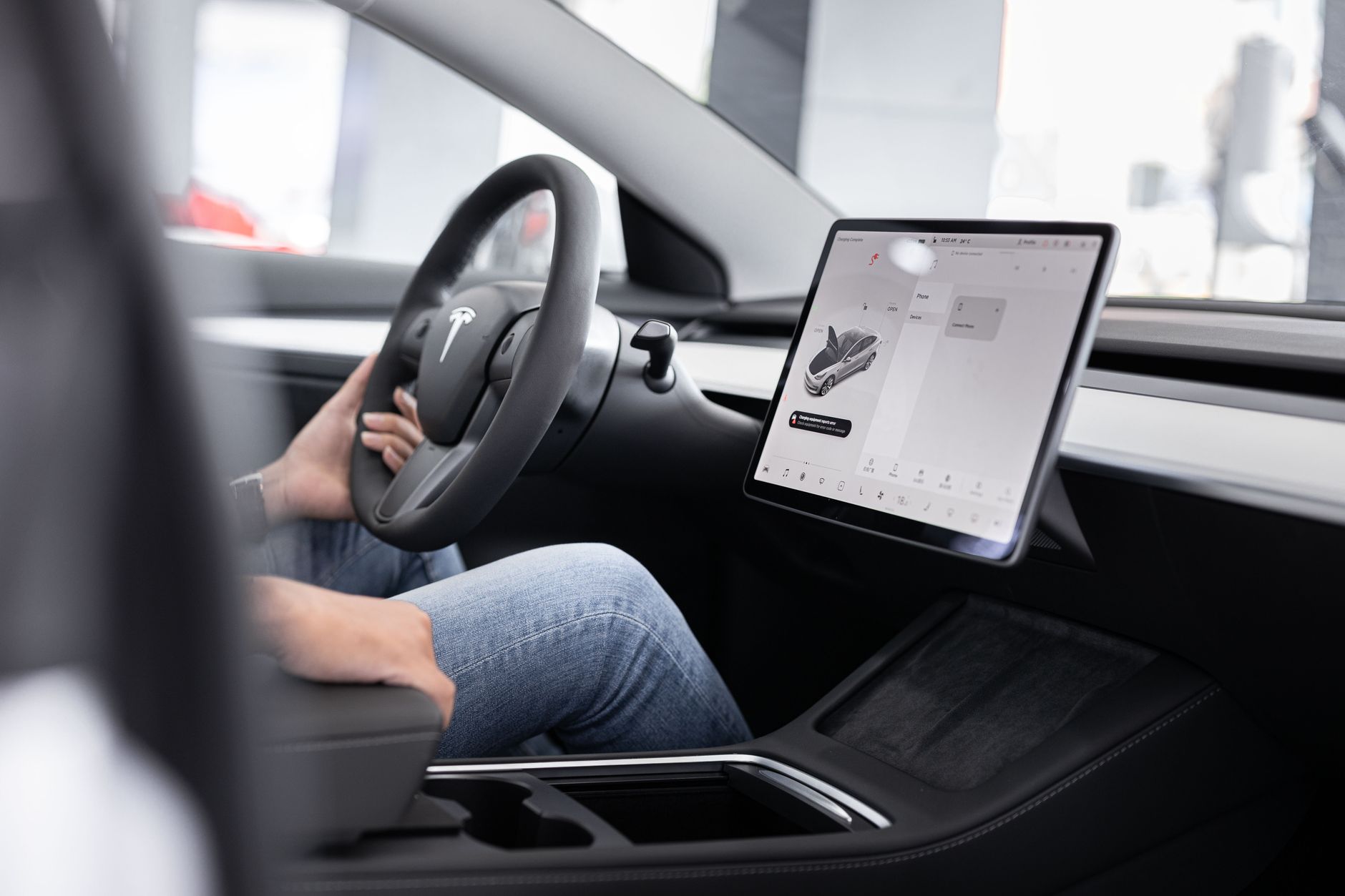 Interior of an electric car showing steering wheel and large touchscreen display, indicating modern technology.