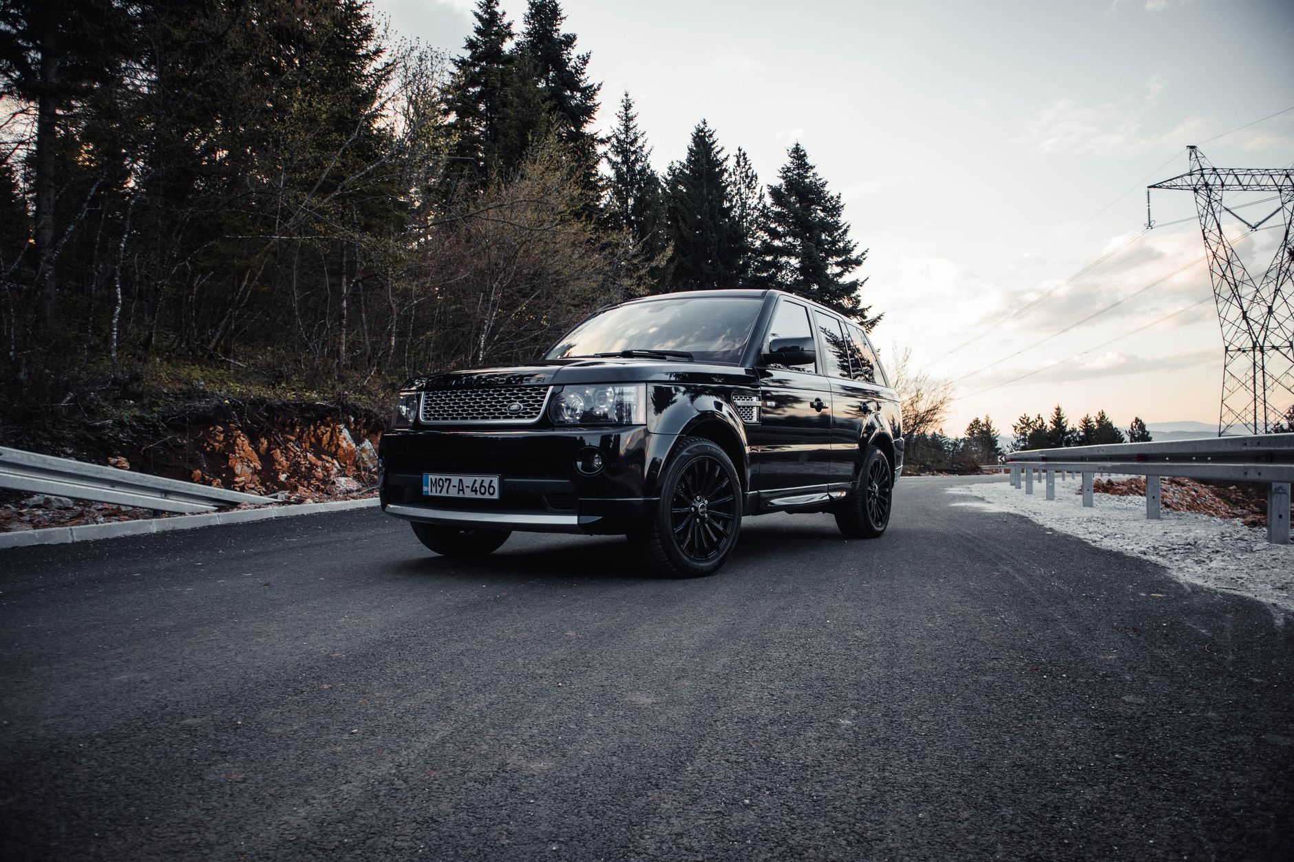 A black luxury SUV drives along a scenic mountain road during sunset near Sarajevo.