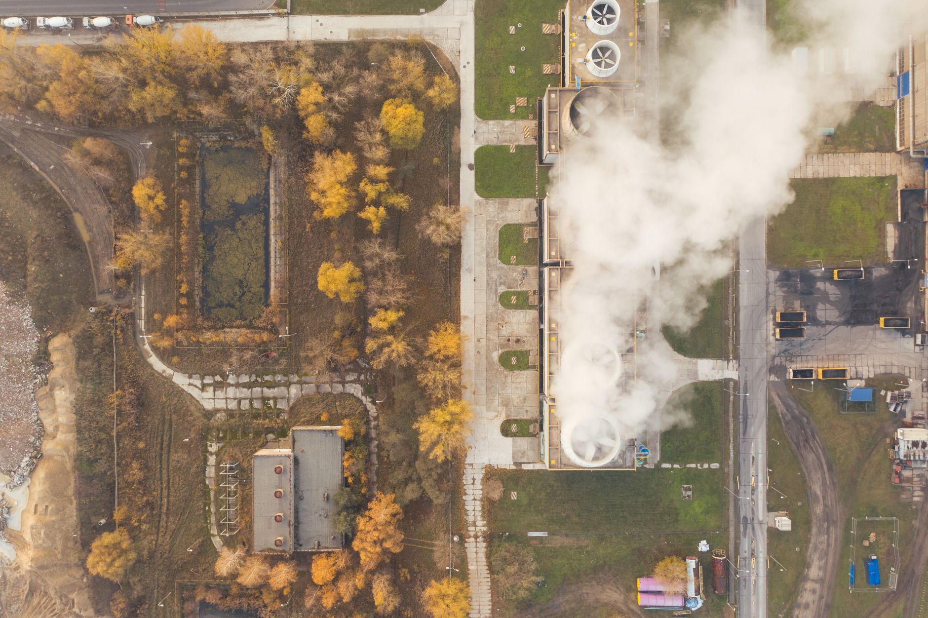 Aerial shot of an industrial plant with smokestacks and surrounding yellow trees in Poznań, Poland.