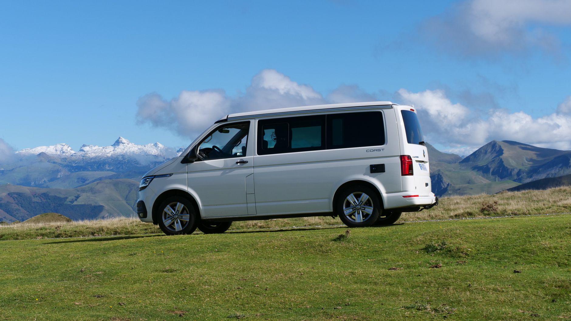 White van parked on a lush green field with stunning mountain background under blue skies.