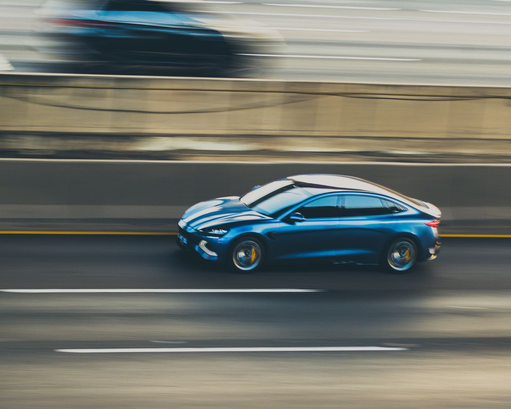 A dynamic panning shot of a sleek blue car speeding down a highway, captured with motion blur.