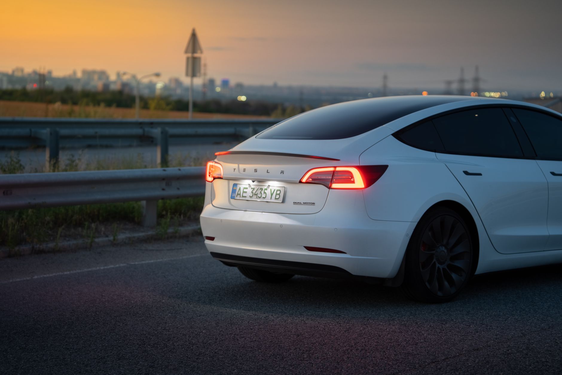 A sleek white electric car on a highway near Dnipro, Ukraine, captured at dusk with city lights in the background.