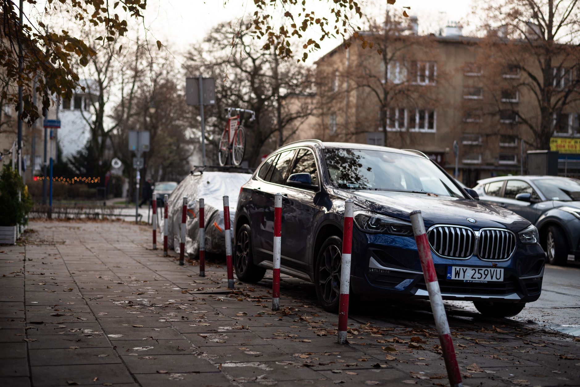 Luxury car parked on a city street with autumn leaves and urban surroundings.