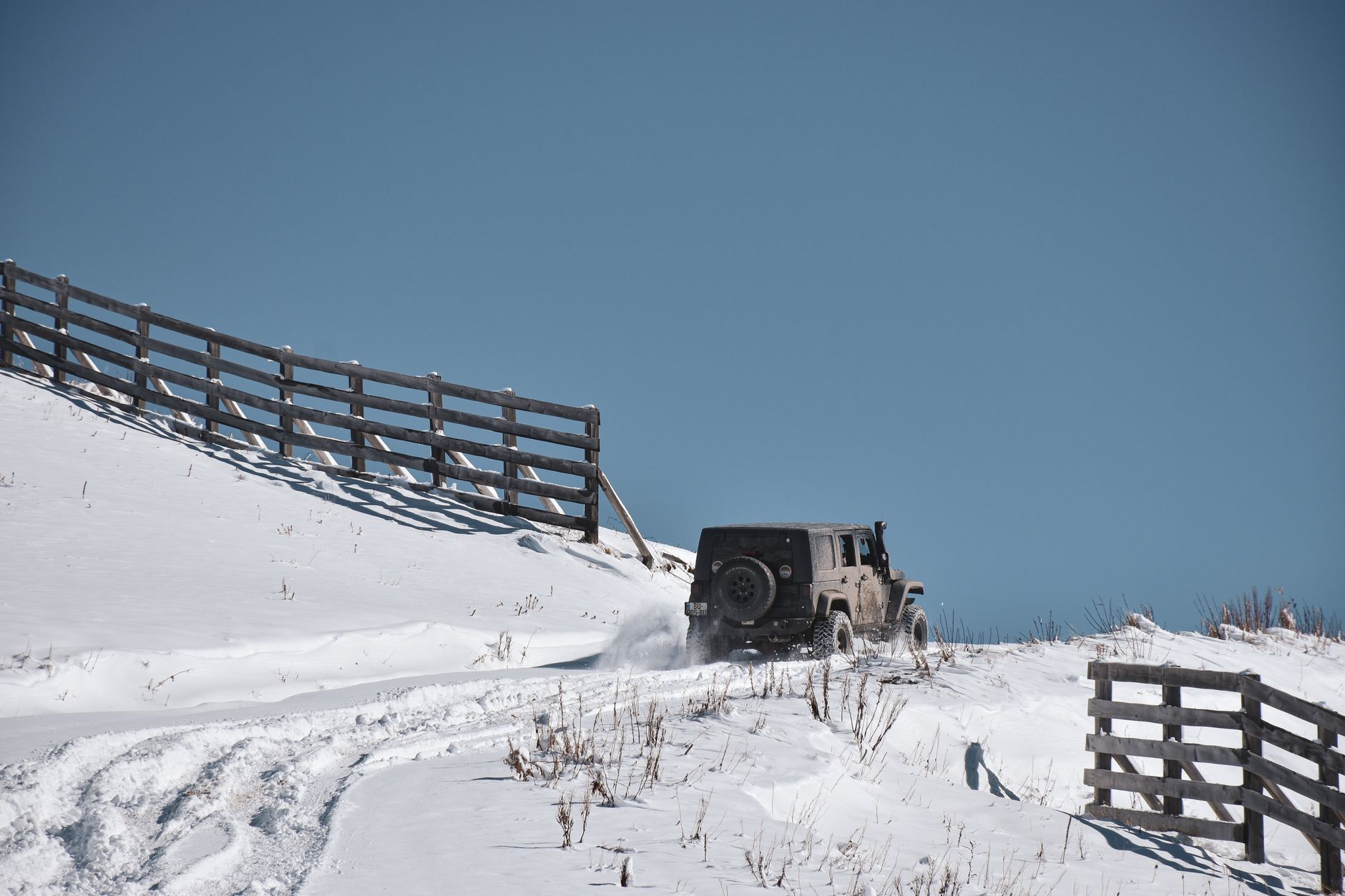 Jeep traversing snowy landscape with wooden fence, capturing winter adventure spirit.
