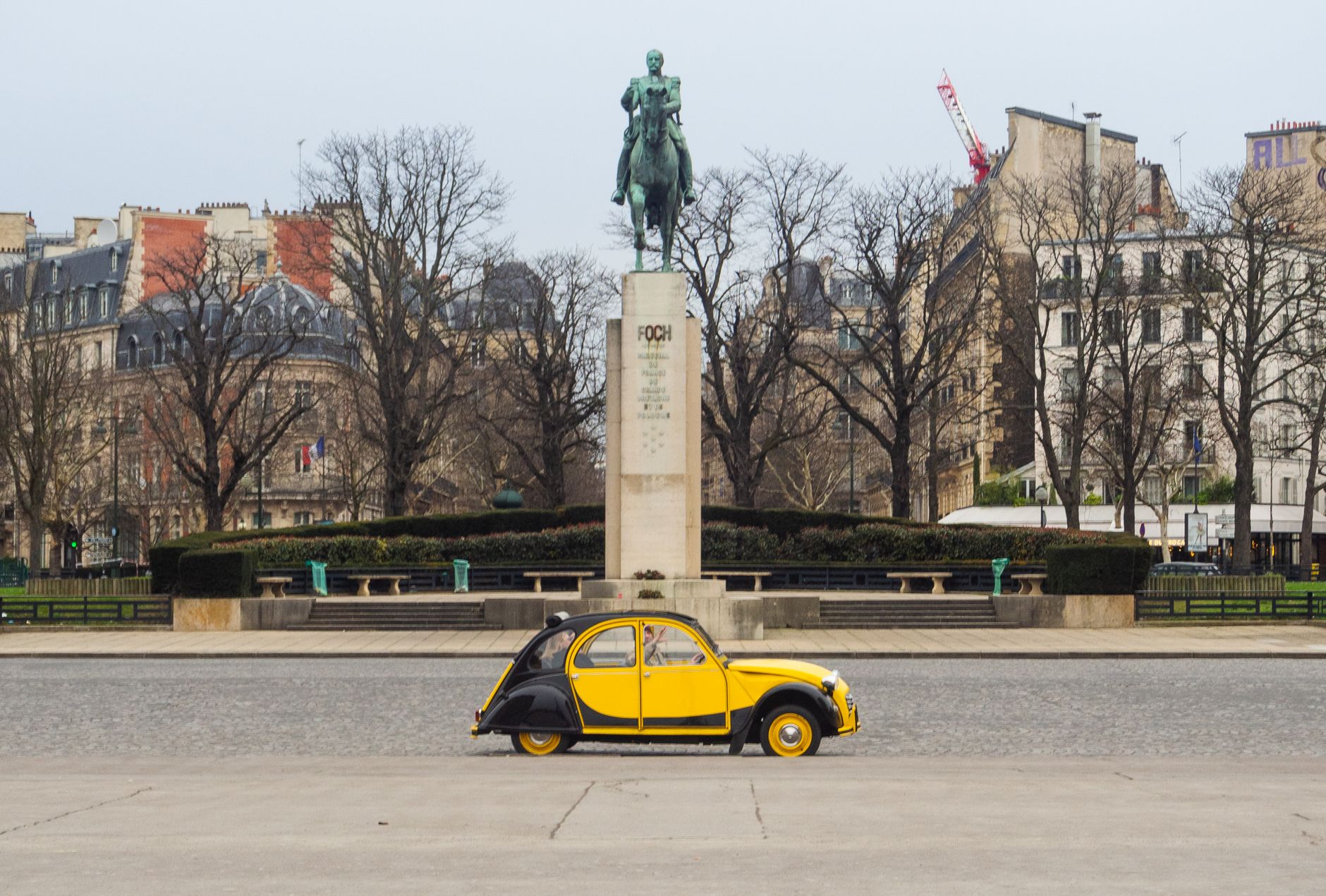 Classic yellow Citroën 2CV in front of the Foch Monument in Paris, capturing a vintage charm.