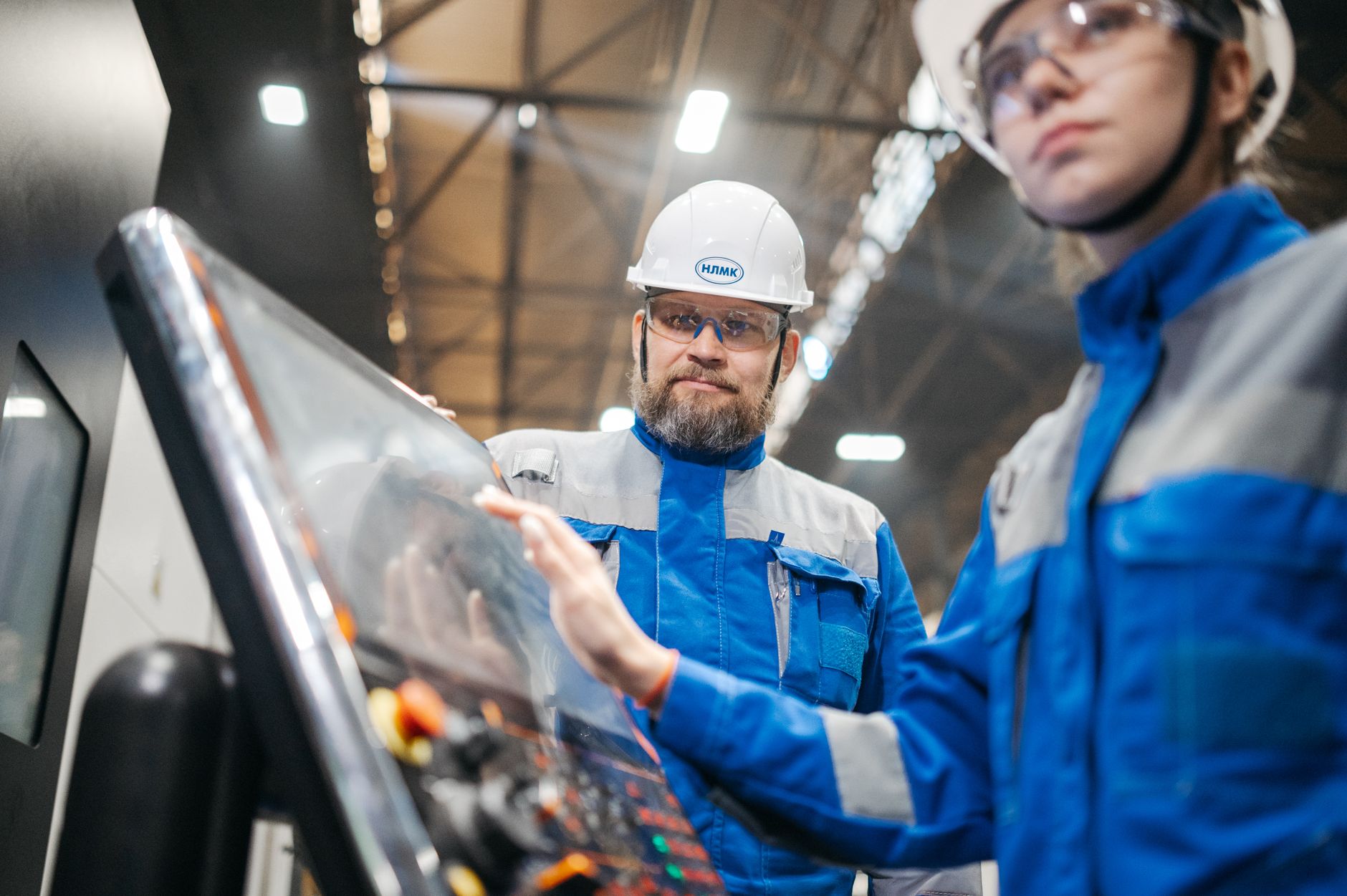 Two industrial workers in safety gear operate machinery in a modern facility.