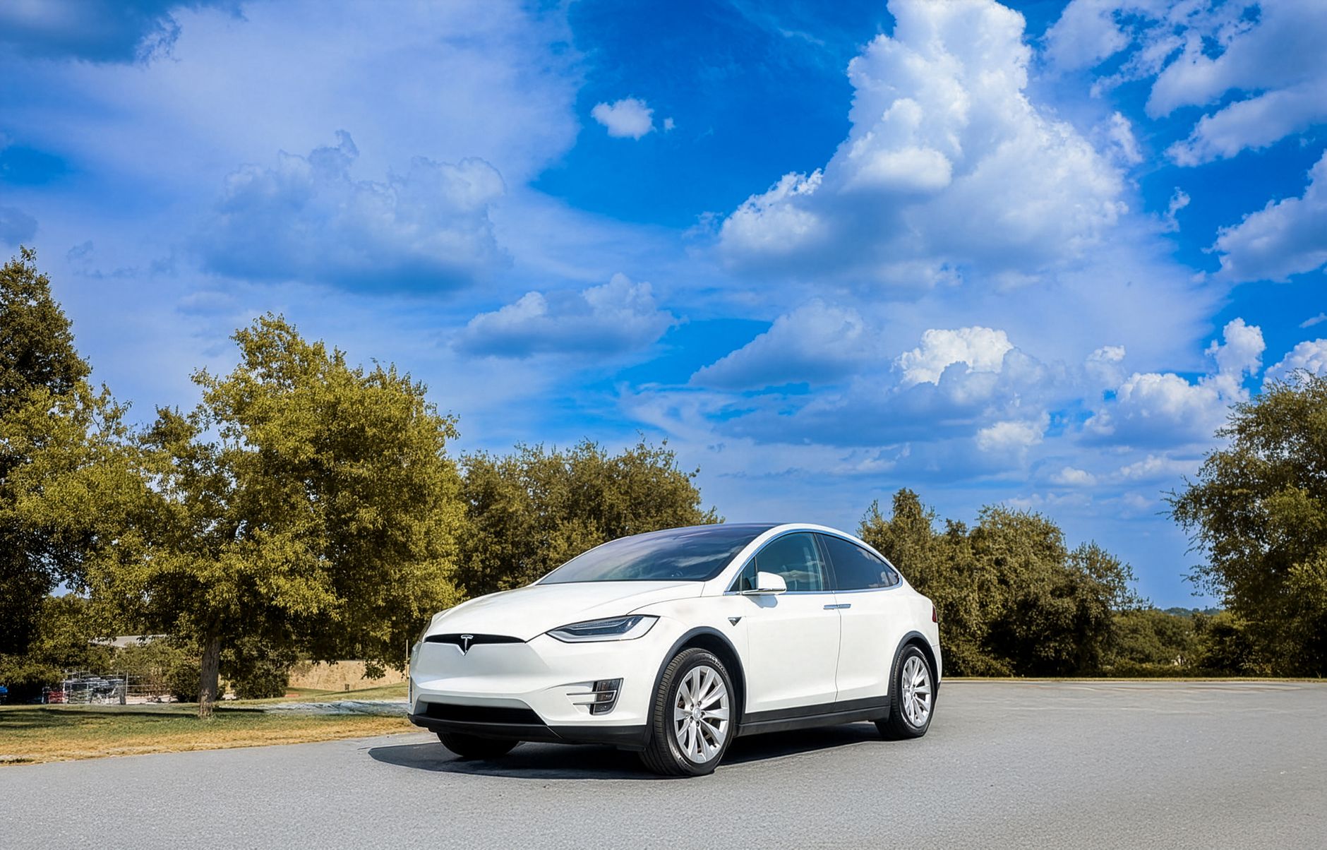 A sleek white electric car parked in a picturesque outdoor landscape with blue skies and fluffy clouds.
