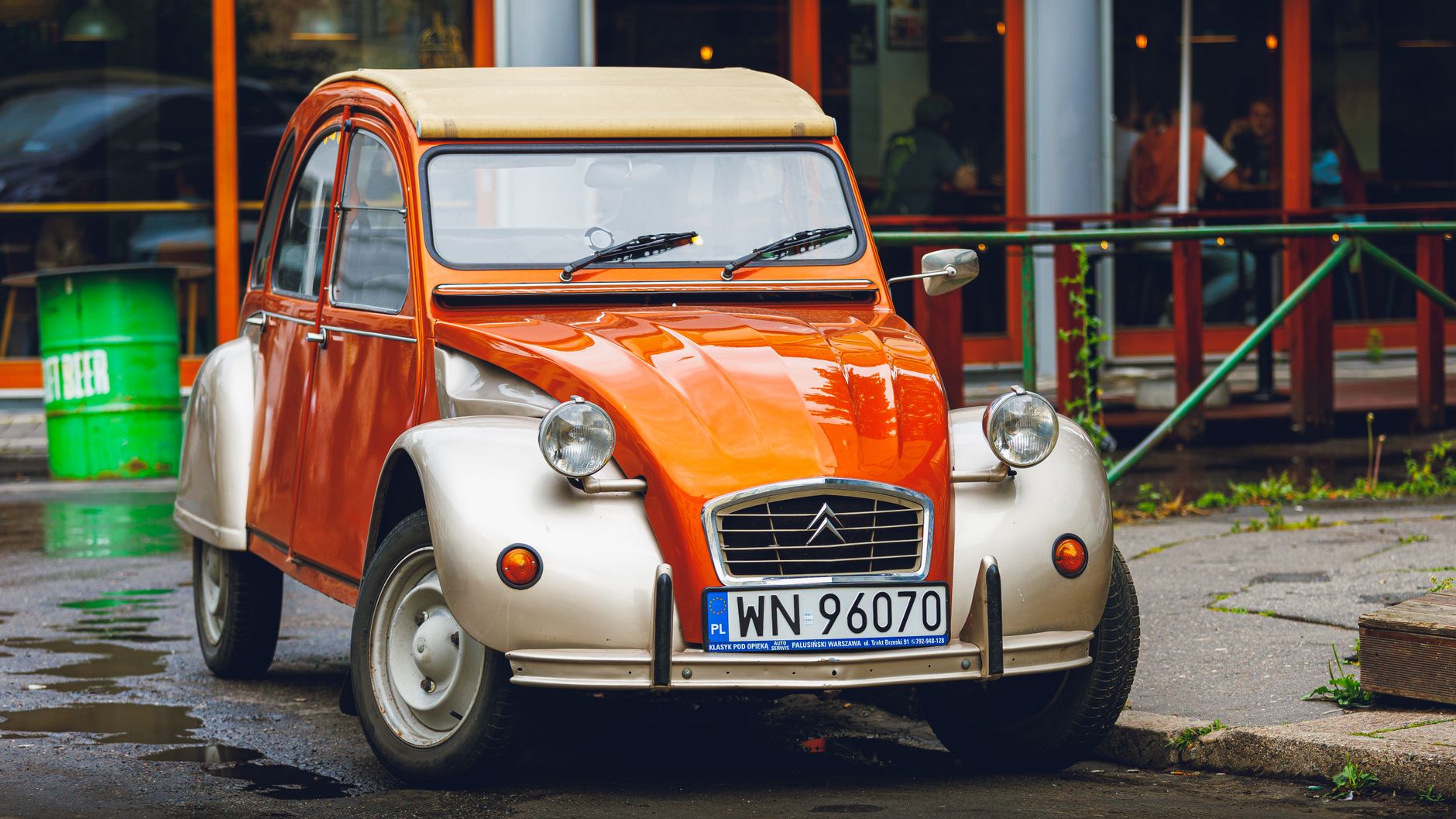 Classic orange and cream Citroën 2CV parked outdoors on a city street.