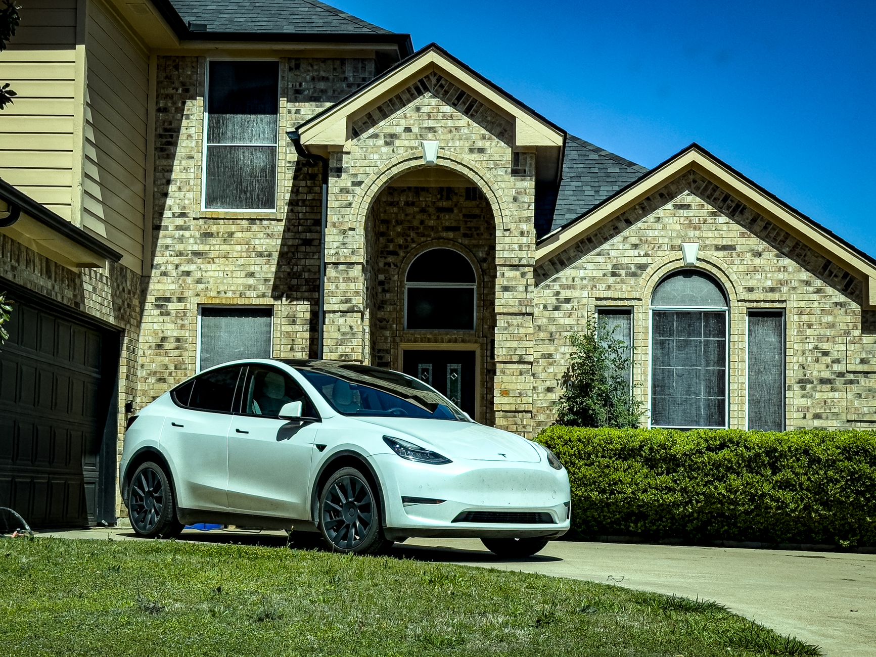 Stylish white electric car parked by a classic brick house in sunny Mansfield, Texas.